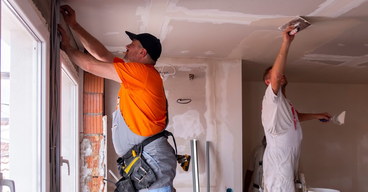 Two crew members on ladders in a home working on spackling the walls and ceiling during a restoration project.