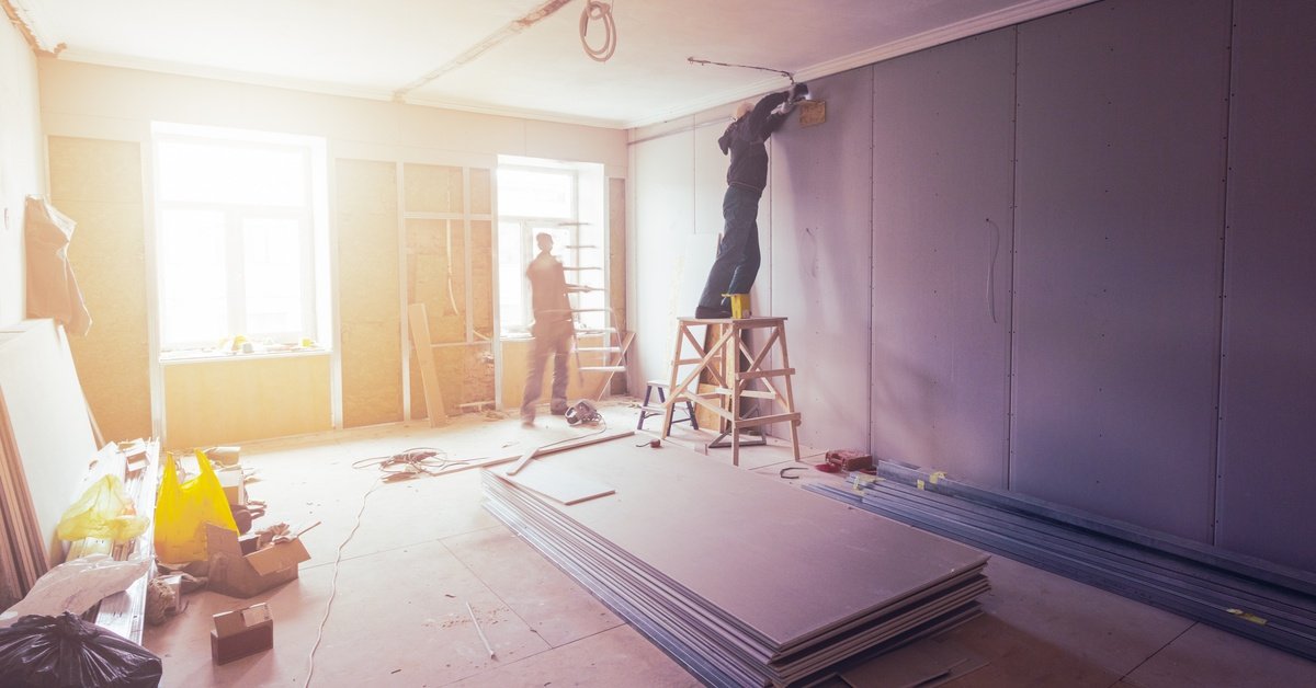  Two crew members working on replacing the drywall inside of a building during a restoration project with light flooding in.